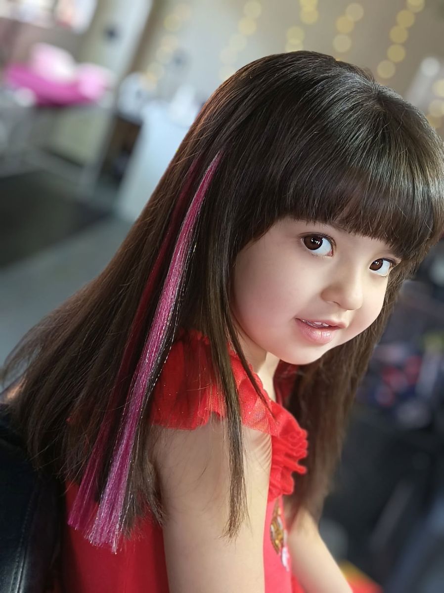 A young client smiling after her haircut with soft pink colour strands at Lynne’s Hair Studio